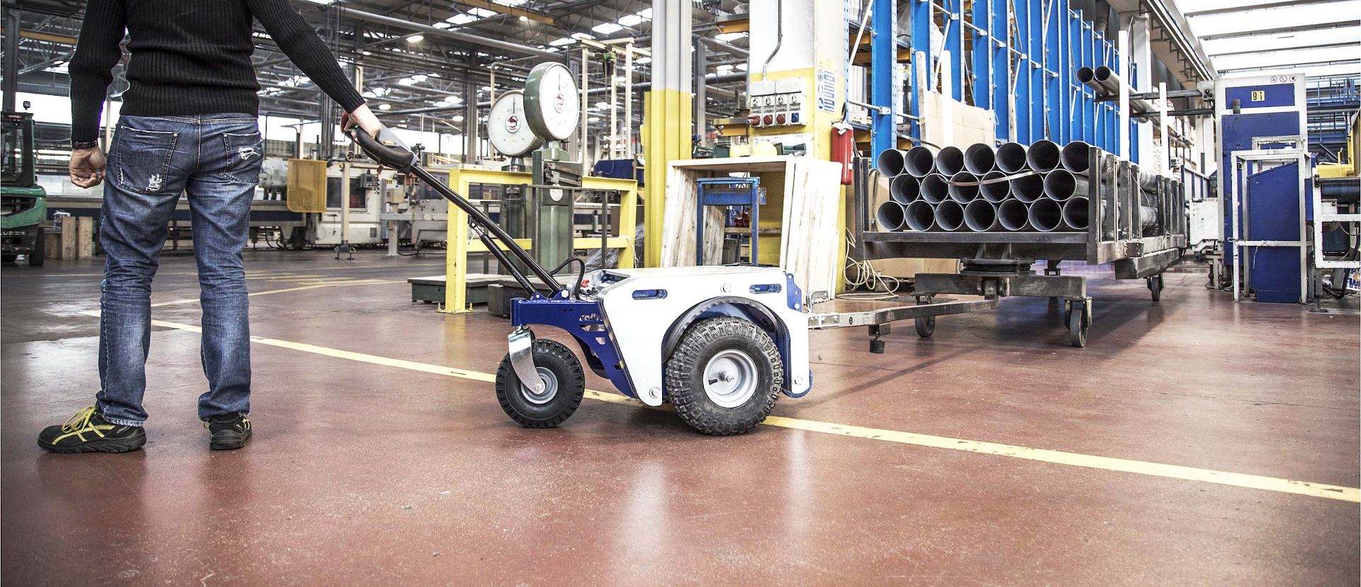 Remorqueur électrique Zallys M4 qui déplaces des chariots à 4 roues transportant tubes en acier dans une industrie manufacturière